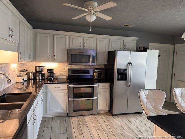 5516 Hall Glen Dr, Hope Mills, NC 28348 - kitchen with appliances with stainless steel finishes, tasteful backsplash, ceiling fan, white cabinetry, and light wood-style floors