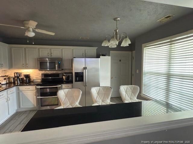 5516 Hall Glen Dr, Hope Mills, NC 28348 - kitchen featuring stainless steel appliances, a chandelier, dark countertops, decorative backsplash, and light wood-style flooring