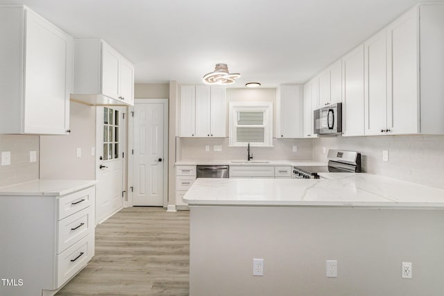 2324 Dahlgreen Rd, Raleigh, NC 27615 - kitchen with appliances with stainless steel finishes, a peninsula, light stone counters, backsplash, and light wood-style flooring