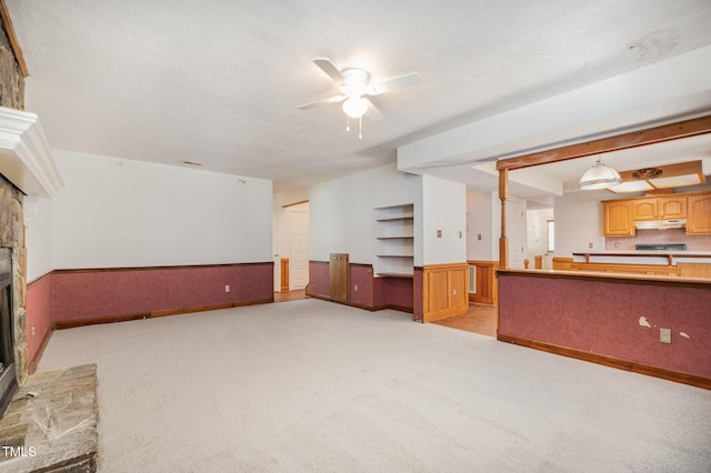 2817 Henslowe Dr, Raleigh, NC 27603 - unfurnished living room featuring a stone fireplace, light colored carpet, wainscoting, and ceiling fan