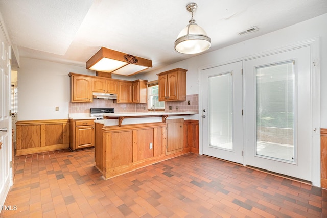 2817 Henslowe Dr, Raleigh, NC 27603 - kitchen with under cabinet range hood, range, light countertops, a wainscoted wall, and a peninsula