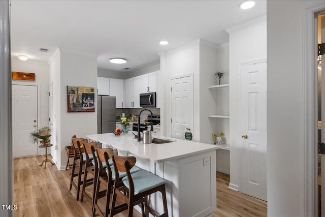 800 Savannah Ridge Rd Unit 109, Holly Springs, NC 27540 - kitchen with appliances with stainless steel finishes, crown molding, a kitchen bar, light wood-type flooring, and light countertops