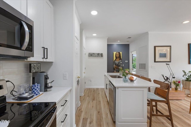 800 Savannah Ridge Rd Unit 109, Holly Springs, NC 27540 - kitchen with appliances with stainless steel finishes, a breakfast bar area, light wood finished floors, white cabinets, and decorative backsplash