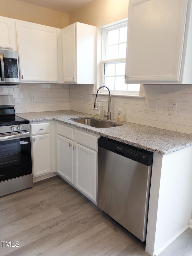7710 River Field Dr, Raleigh, NC 27616 - kitchen featuring stainless steel appliances, a sink, white cabinets, light wood-style floors, and tasteful backsplash