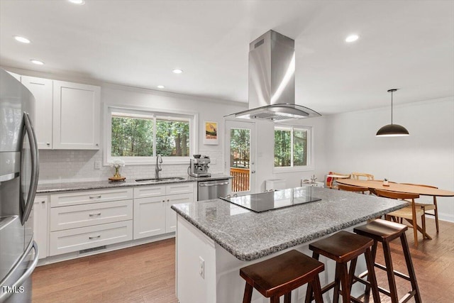6609 Hunters Ln, Durham, NC 27713 - kitchen featuring island exhaust hood, stainless steel appliances, ornamental molding, wood finished floors, and a breakfast bar area