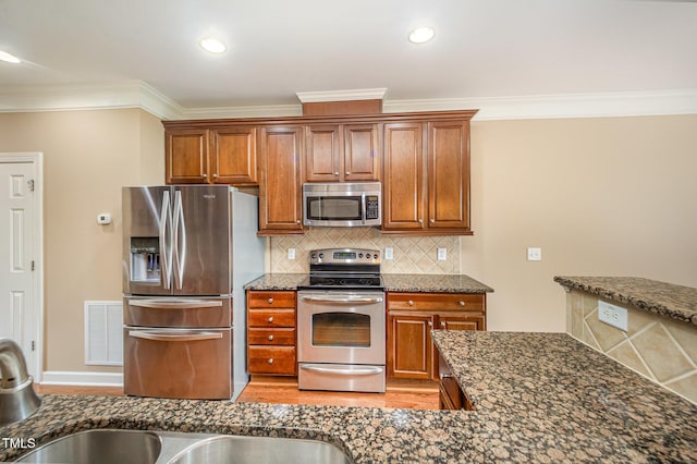 404 Panorama Park Pl, Cary, NC 27519 - kitchen with appliances with stainless steel finishes, ornamental molding, light wood finished floors, dark stone countertops, and brown cabinetry