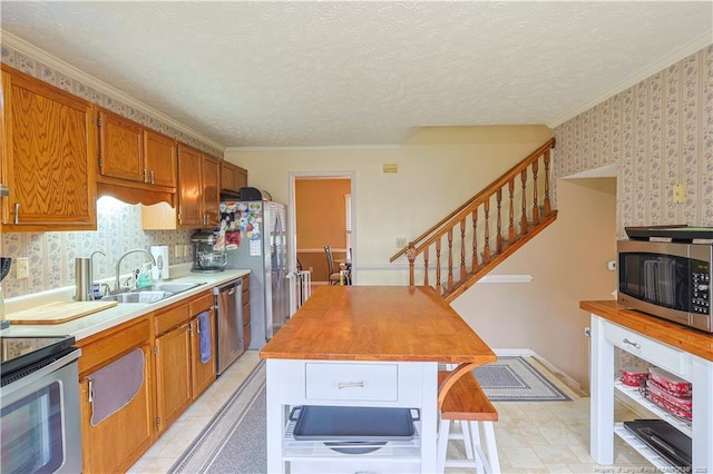 874 Santiato Dr, Fayetteville, NC 28314 - kitchen featuring appliances with stainless steel finishes, wallpapered walls, a sink, brown cabinetry, and crown molding