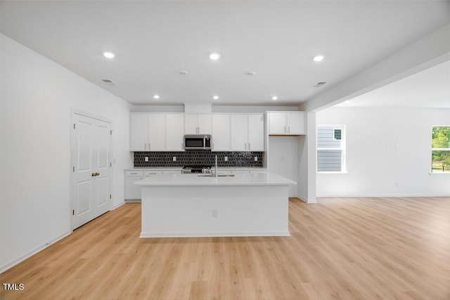 1061 Hardin Hill Ln, Knightdale, NC 27545 - kitchen featuring stainless steel microwave, white cabinets, a kitchen island with sink, decorative backsplash, and recessed lighting