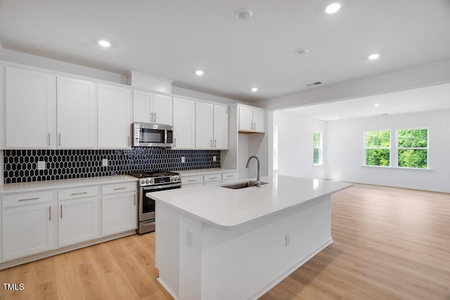 1061 Hardin Hill Ln, Knightdale, NC 27545 - kitchen with appliances with stainless steel finishes, light wood finished floors, white cabinetry, decorative backsplash, and a center island with sink