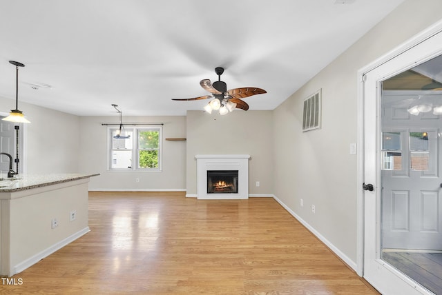 3427 Mill Run, Raleigh, NC 27612 - unfurnished living room featuring ceiling fan, light wood-type flooring, a warm lit fireplace, baseboards, and a sink