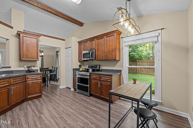 5801 Hadrian Dr, Durham, NC 27703 - kitchen featuring appliances with stainless steel finishes, dark countertops, wood finished floors, brown cabinetry, and hanging light fixtures