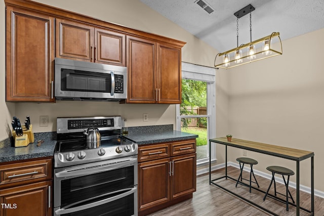 5801 Hadrian Dr, Durham, NC 27703 - kitchen featuring appliances with stainless steel finishes, lofted ceiling, dark countertops, wood finished floors, and hanging light fixtures