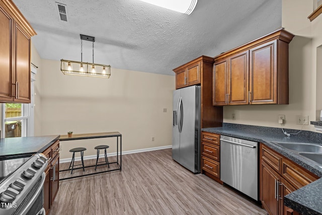 5801 Hadrian Dr, Durham, NC 27703 - kitchen with appliances with stainless steel finishes, dark countertops, light wood finished floors, brown cabinets, and hanging light fixtures