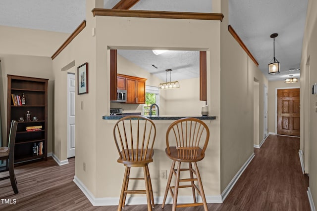 5801 Hadrian Dr, Durham, NC 27703 - kitchen featuring stainless steel microwave, dark wood-style floors, brown cabinets, a textured ceiling, and pendant lighting
