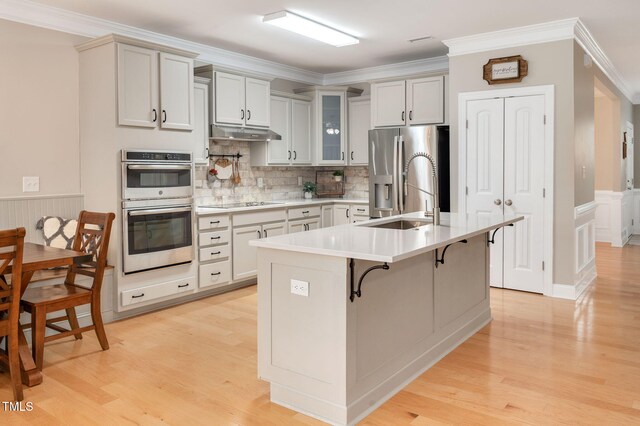 5637 Garnet Meadow Rd, Knightdale, NC 27545 - kitchen with appliances with stainless steel finishes, under cabinet range hood, a breakfast bar, light wood-type flooring, and crown molding