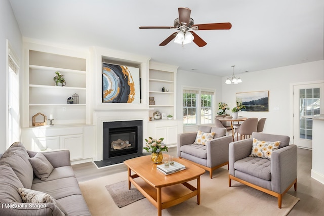 1148 Dexter Ridge Dr, Holly Springs, NC 27540 - living area with light wood-style flooring, a chandelier, a ceiling fan, a glass covered fireplace, and built in features