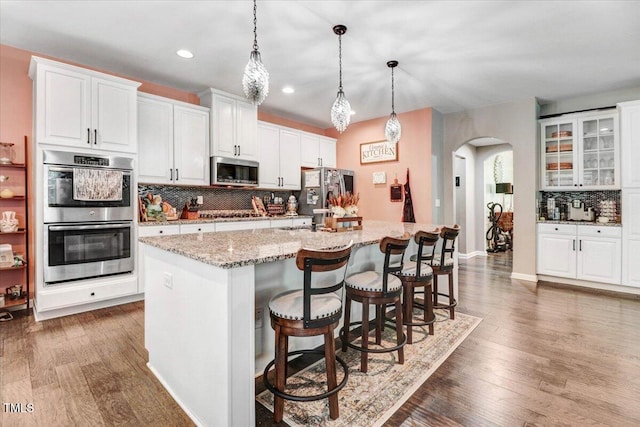 728 Opposition Way, Wake Forest, NC 27587 - kitchen with appliances with stainless steel finishes, arched walkways, tasteful backsplash, an island with sink, and white cabinets