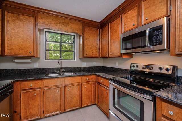 2629 Hiking Trl, Raleigh, NC 27615 - kitchen with stainless steel appliances, brown cabinets, dark stone counters, light tile patterned floors, and a textured ceiling