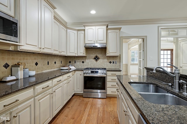 1217 Chalk Maple Dr, Cary, NC 27519 - kitchen featuring appliances with stainless steel finishes, light wood-type flooring, under cabinet range hood, dark stone counters, and tasteful backsplash