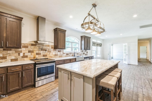 589 Atkinson Mill Rd, Selma, NC 27576 - kitchen with stainless steel electric stove, wall chimney exhaust hood, a breakfast bar area, a center island, and light wood-style flooring