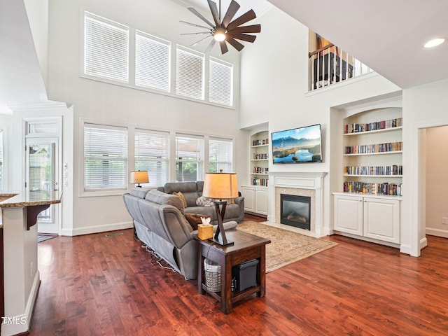 214 Ashdown Forest Ln, Cary, NC 27519 - living room featuring ceiling fan, a towering ceiling, a fireplace with flush hearth, dark wood-style floors, and built in shelves