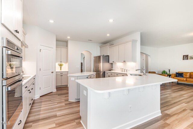 124 Airlie Place Ln, Willow Springs, NC 27592 - kitchen with arched walkways, appliances with stainless steel finishes, light wood-type flooring, a kitchen island, and tasteful backsplash
