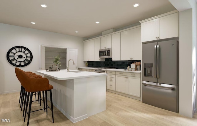 1216 Hardin Hill Ln, Knightdale, NC 27545 - kitchen featuring appliances with stainless steel finishes, a center island with sink, light wood finished floors, decorative backsplash, and white cabinetry