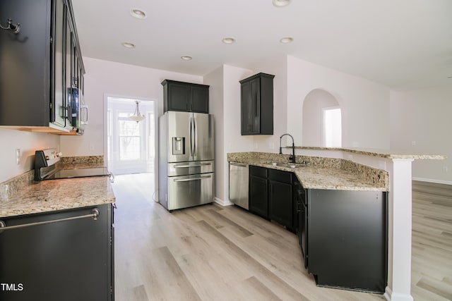 616 Cheselden Dr, Durham, NC 27713 - kitchen featuring appliances with stainless steel finishes, a peninsula, light wood finished floors, light stone countertops, and arched walkways