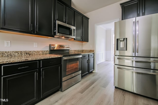 616 Cheselden Dr, Durham, NC 27713 - kitchen with stainless steel appliances, dark cabinetry, light wood-style floors, wainscoting, and light stone counters