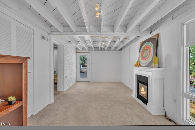 3205 Dell Dr, Raleigh, NC 27609 - unfurnished living room featuring healthy amount of natural light, a glass covered fireplace, light colored carpet, brick wall, and beamed ceiling