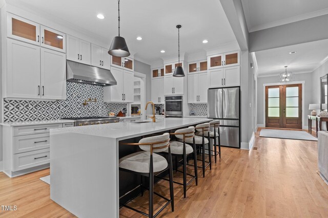 310 Hidden Lake Dr, Youngsville, NC 27596 - kitchen featuring appliances with stainless steel finishes, under cabinet range hood, ornamental molding, a center island with sink, and light wood finished floors
