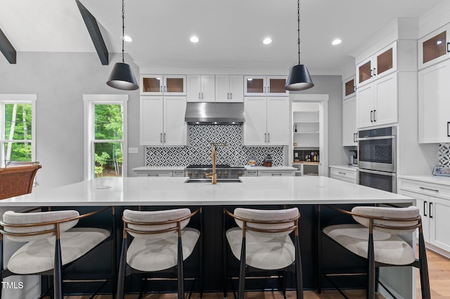 310 Hidden Lake Dr, Youngsville, NC 27596 - kitchen featuring under cabinet range hood, double oven, backsplash, light countertops, and a center island with sink