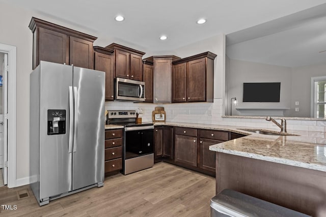 244 Lasswade Ct, Zebulon, NC 27597 - kitchen featuring stainless steel appliances, light stone countertops, light wood-style flooring, dark brown cabinetry, and recessed lighting