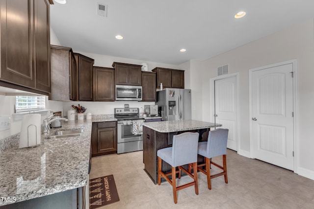 525 Willow Breeze Ct, Zebulon, NC 27597 - kitchen featuring stainless steel appliances, a breakfast bar area, dark brown cabinets, a kitchen island, and light stone countertops