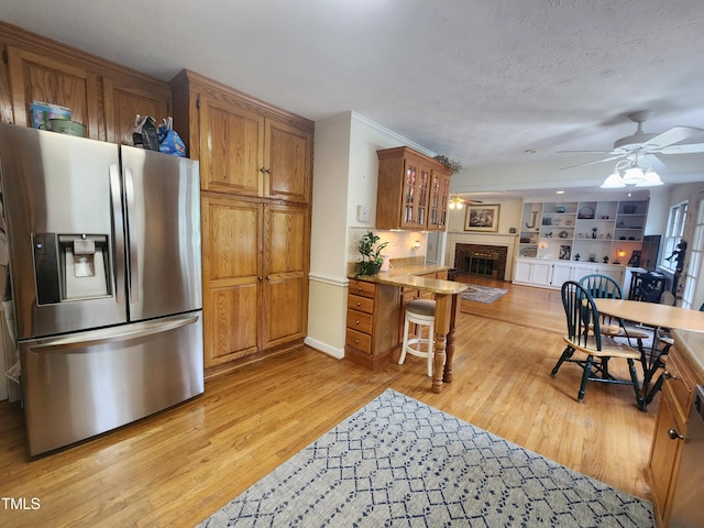 5760 Hesters Store Rd, Hurdle Mills, NC 27541 - kitchen featuring stainless steel fridge with ice dispenser, a ceiling fan, a fireplace, brown cabinets, and glass insert cabinets