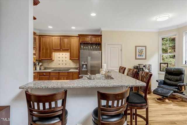 218 Kinvara Ct, Wake Forest, NC 27587 - kitchen with stainless steel refrigerator with ice dispenser, ornamental molding, brown cabinets, a breakfast bar area, and recessed lighting