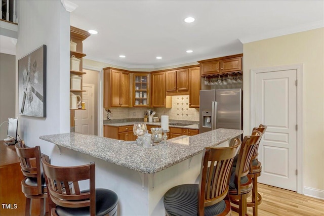 218 Kinvara Ct, Wake Forest, NC 27587 - kitchen with stainless steel fridge with ice dispenser, brown cabinetry, light wood finished floors, backsplash, and glass insert cabinets