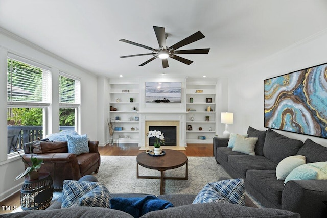 101 Ironcreek Pl, Apex, NC 27539 - living room featuring ornamental molding, ceiling fan, wood finished floors, a fireplace with flush hearth, and built in shelves