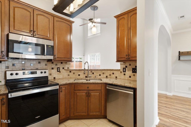 1016 Goldmist Ln, Durham, NC 27713 - kitchen with appliances with stainless steel finishes, ornamental molding, a ceiling fan, light stone countertops, and brown cabinetry