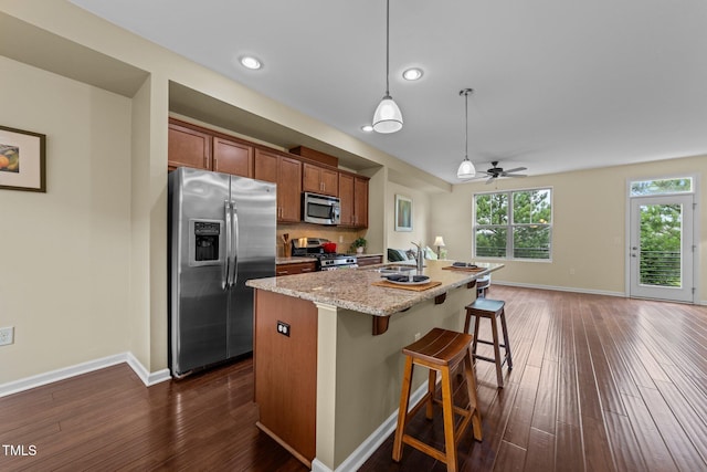 4124 Sykes St, Cary, NC 27519 - kitchen featuring appliances with stainless steel finishes, dark wood finished floors, brown cabinets, a kitchen bar, and a center island with sink