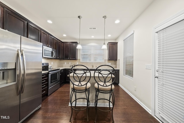 7235 Terregles Dr, Raleigh, NC 27617 - kitchen featuring stainless steel appliances, dark brown cabinets, dark wood-style floors, tasteful backsplash, and a breakfast bar