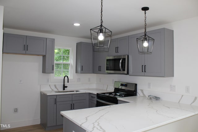 4511 Denfield St, Durham, NC 27704 - kitchen with stainless steel appliances, a peninsula, gray cabinetry, light stone counters, and hanging light fixtures