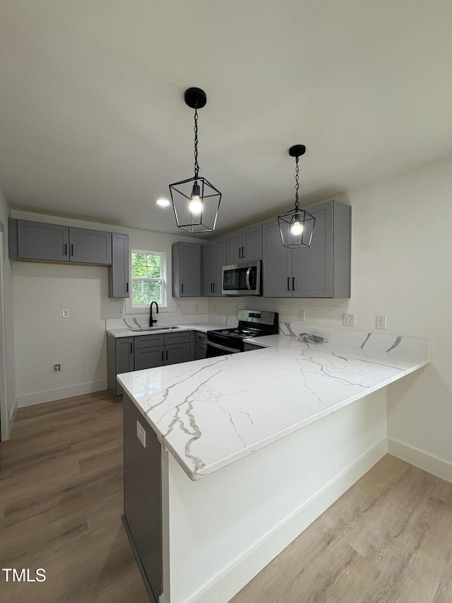 4511 Denfield St, Durham, NC 27704 - kitchen with stainless steel microwave, stove, gray cabinetry, a peninsula, and light stone countertops