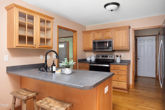 404 Denton St, Durham, NC 27713 - kitchen featuring stainless steel appliances, dark countertops, a peninsula, light wood finished floors, and glass insert cabinets