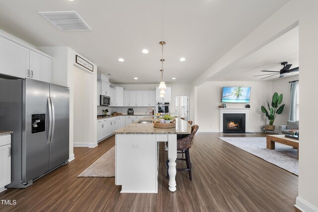 433 Village Bend Dr, Fuquay Varina, NC 27526 - kitchen featuring appliances with stainless steel finishes, open floor plan, dark wood-style flooring, a fireplace with flush hearth, and light stone countertops