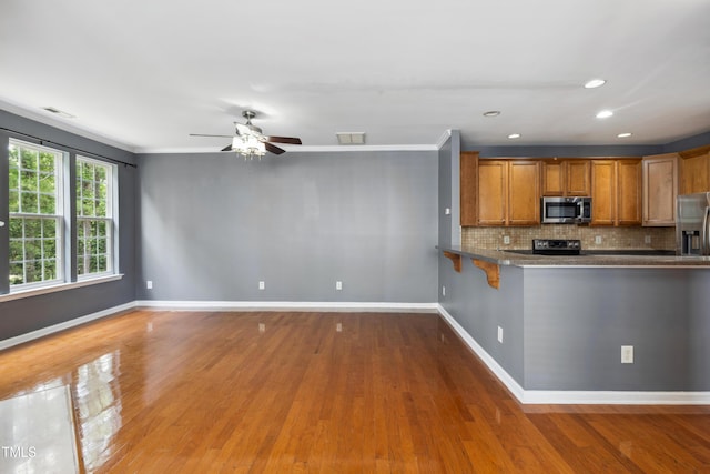 5503 Silver Moon Ln, Raleigh, NC 27606 - kitchen with appliances with stainless steel finishes, brown cabinets, wood finished floors, ceiling fan, and tasteful backsplash