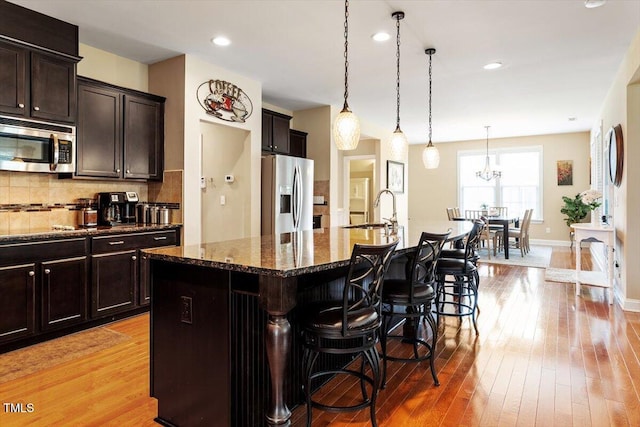 150 Saint Mellion St, Raleigh, NC 27603 - kitchen with appliances with stainless steel finishes, tasteful backsplash, a kitchen island with sink, a kitchen bar, and light wood-type flooring