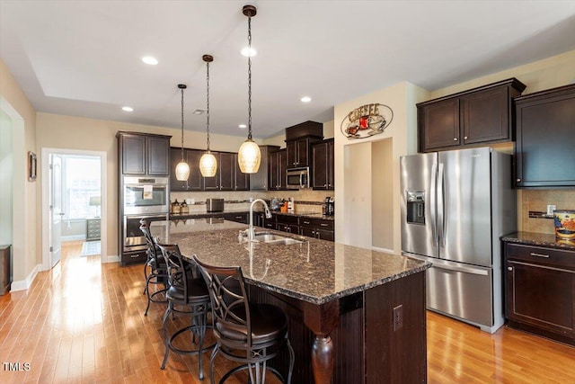 150 Saint Mellion St, Raleigh, NC 27603 - kitchen featuring appliances with stainless steel finishes, light wood-style flooring, dark brown cabinets, a kitchen bar, and dark stone counters