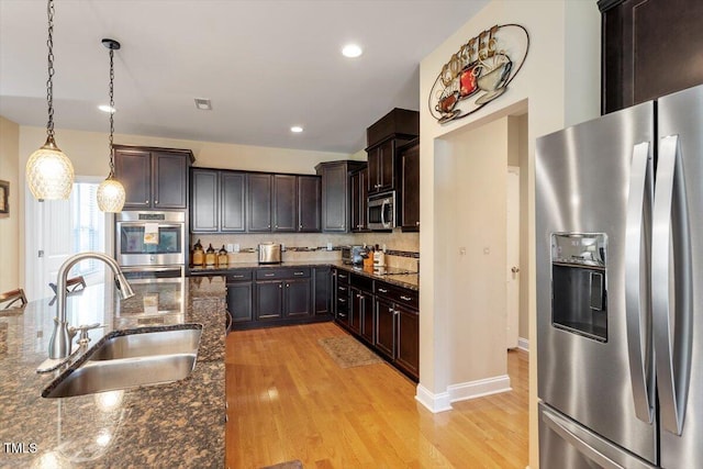 150 Saint Mellion St, Raleigh, NC 27603 - kitchen with appliances with stainless steel finishes, light wood-type flooring, dark brown cabinetry, dark stone counters, and hanging light fixtures