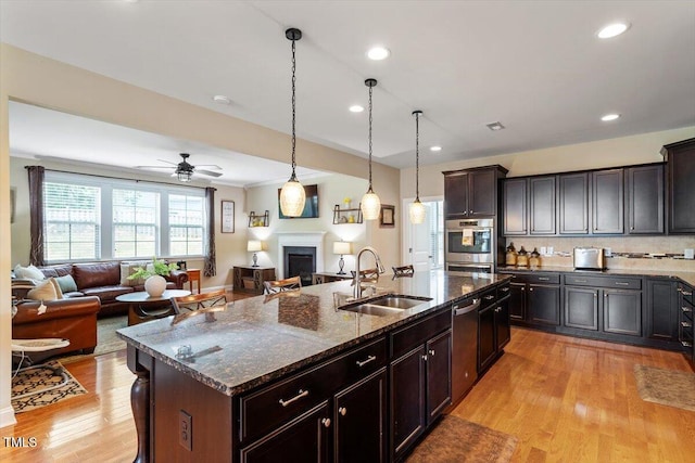 150 Saint Mellion St, Raleigh, NC 27603 - kitchen with stainless steel appliances, open floor plan, a center island with sink, a fireplace, and dark stone counters